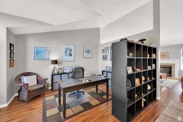 office space featuring a fireplace, vaulted ceiling, wood finished floors, and baseboards