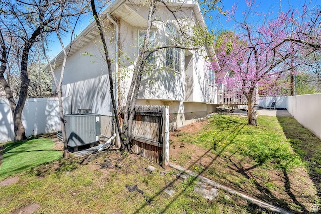 view of side of property featuring central air condition unit, a fenced backyard, and stucco siding