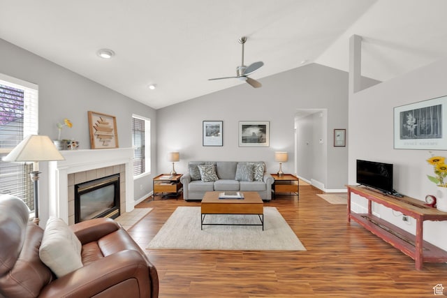 living area with vaulted ceiling, baseboards, wood finished floors, ceiling fan, and a fireplace