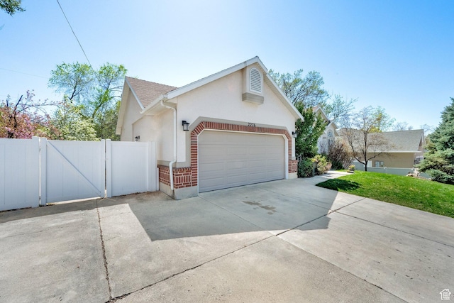view of side of home with a gate, driveway, an attached garage, stucco siding, and brick siding