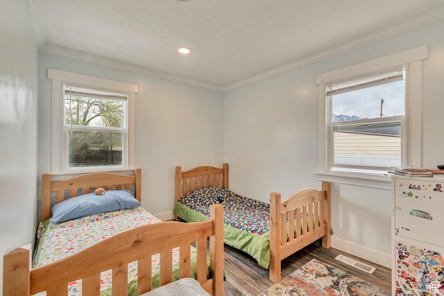 bedroom featuring wood finished floors, visible vents, crown molding, and baseboards