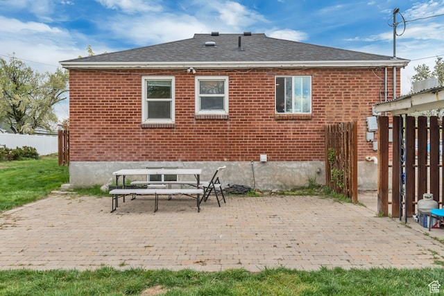 back of property with fence, a patio area, roof with shingles, and brick siding