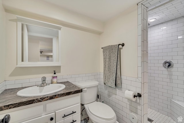 bathroom with vanity, tile walls, a wainscoted wall, toilet, and tiled shower