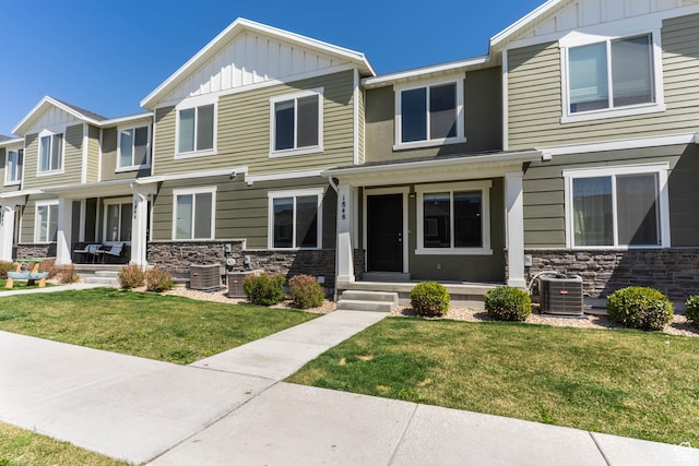 view of front facade featuring board and batten siding, central air condition unit, stone siding, and a front yard