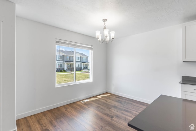 unfurnished dining area featuring visible vents, baseboards, wood finished floors, and an inviting chandelier