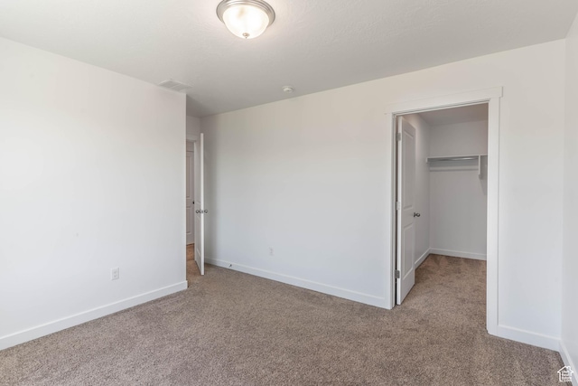 unfurnished bedroom featuring baseboards, visible vents, a closet, carpet floors, and a walk in closet