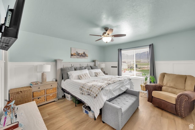 4104 Rose Springs Rd Unit 406, Erda, UT 84074 - bedroom featuring a ceiling fan, a decorative wall, wainscoting, light wood-style flooring, and a textured ceiling
