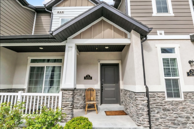 view of exterior entry with stucco siding, stone siding, covered porch, and board and batten siding
