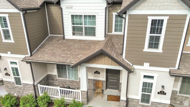 exterior space featuring stone siding and a shingled roof