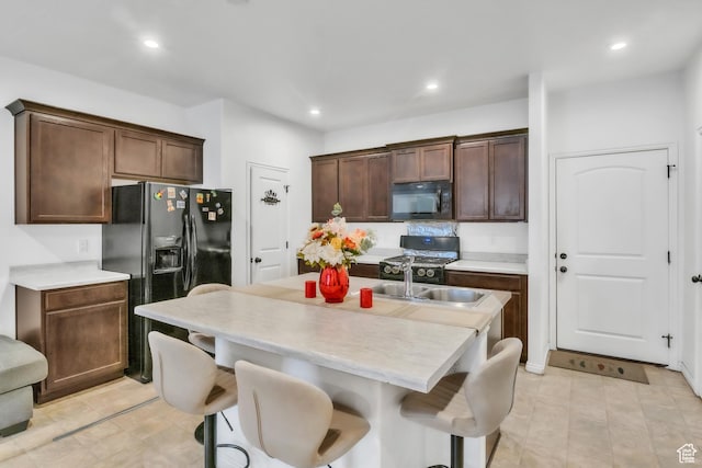kitchen featuring black appliances, an island with sink, a sink, and light countertops