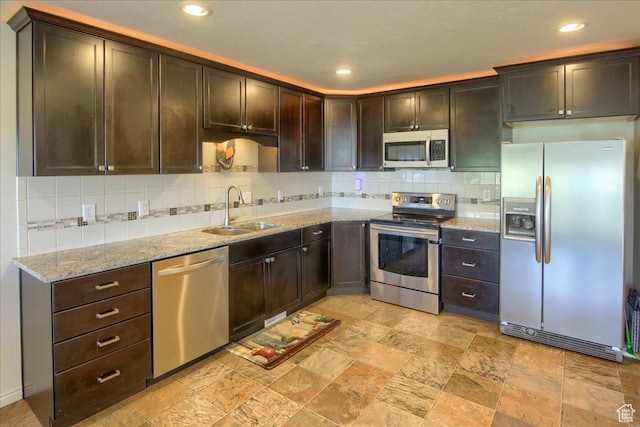 kitchen featuring backsplash, dark brown cabinets, a sink, stone finish flooring, and appliances with stainless steel finishes