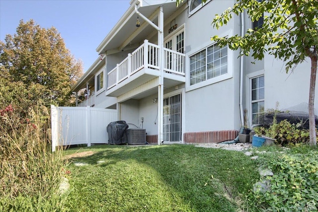 view of side of home with a lawn, central AC unit, a balcony, and stucco siding