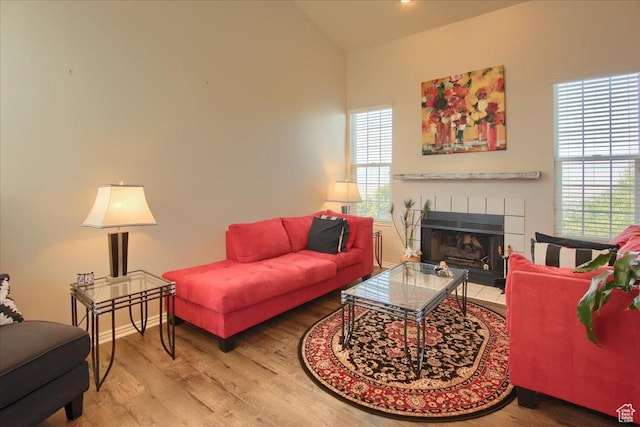 living area featuring baseboards, a tiled fireplace, wood finished floors, and vaulted ceiling