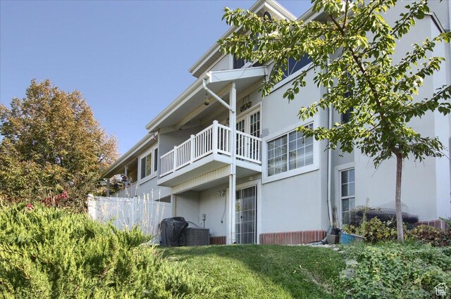 back of house with stucco siding, fence, a balcony, and a lawn