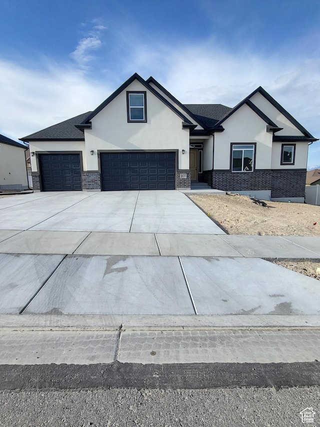 modern farmhouse featuring brick siding, an attached garage, stucco siding, and driveway