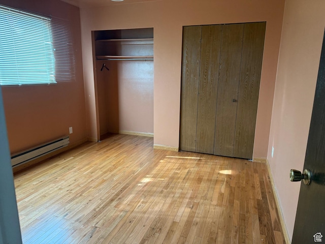 unfurnished bedroom featuring hardwood / wood-style floors, baseboards, two closets, and a baseboard radiator