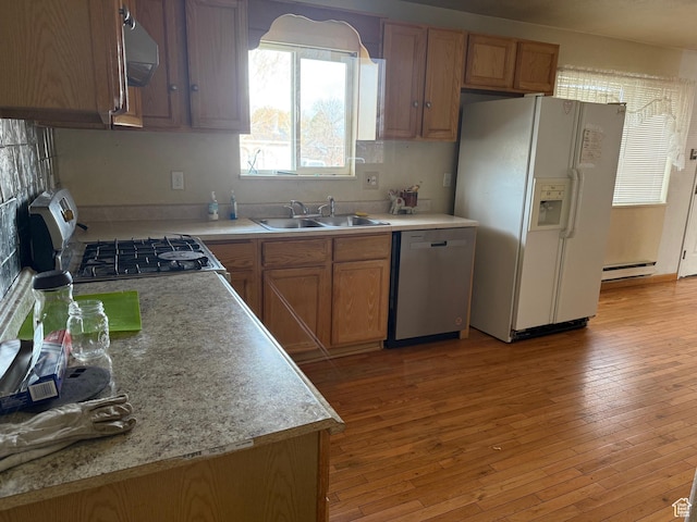 kitchen featuring a baseboard radiator, stainless steel dishwasher, range with gas stovetop, a sink, and white fridge with ice dispenser