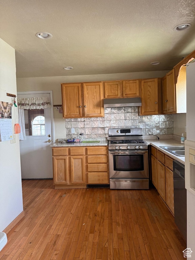 kitchen with exhaust hood, light countertops, dishwasher, stainless steel gas range, and hardwood / wood-style flooring