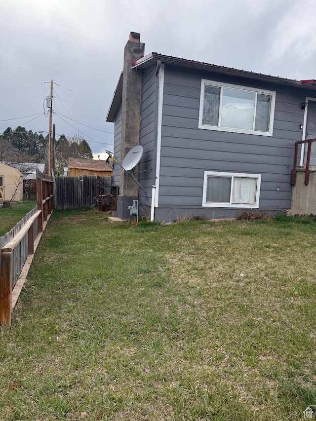 view of home's exterior with a yard, a chimney, and fence