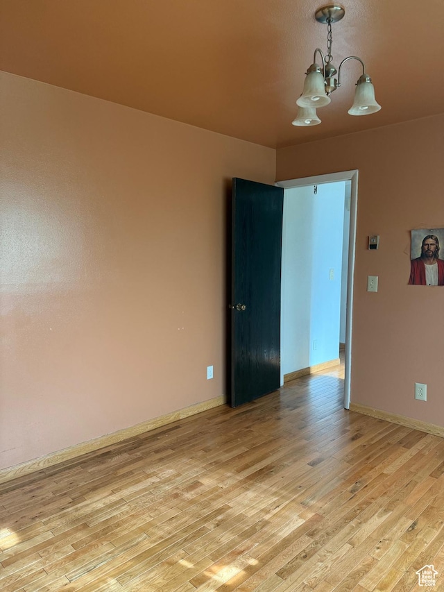 empty room with light wood finished floors, baseboards, and an inviting chandelier