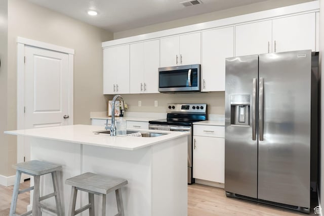 kitchen with a sink, white cabinetry, light wood-style floors, light countertops, and appliances with stainless steel finishes
