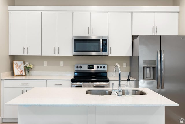 kitchen with white cabinets, light stone counters, stainless steel appliances, a sink, and a center island with sink