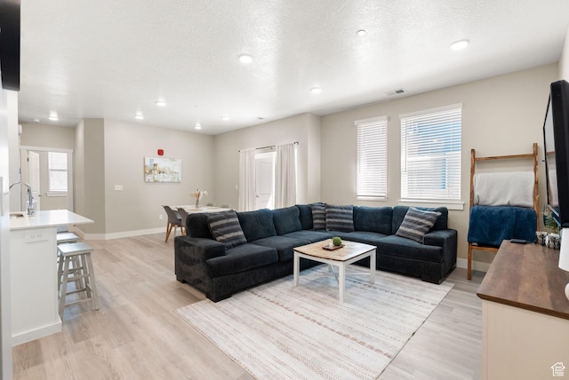living area featuring light wood-type flooring, baseboards, visible vents, and a textured ceiling