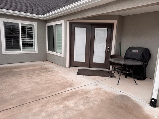 property entrance featuring stucco siding, roof with shingles, and a patio