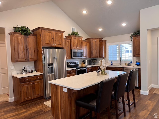 kitchen with vaulted ceiling, appliances with stainless steel finishes, dark wood-style floors, and a breakfast bar area