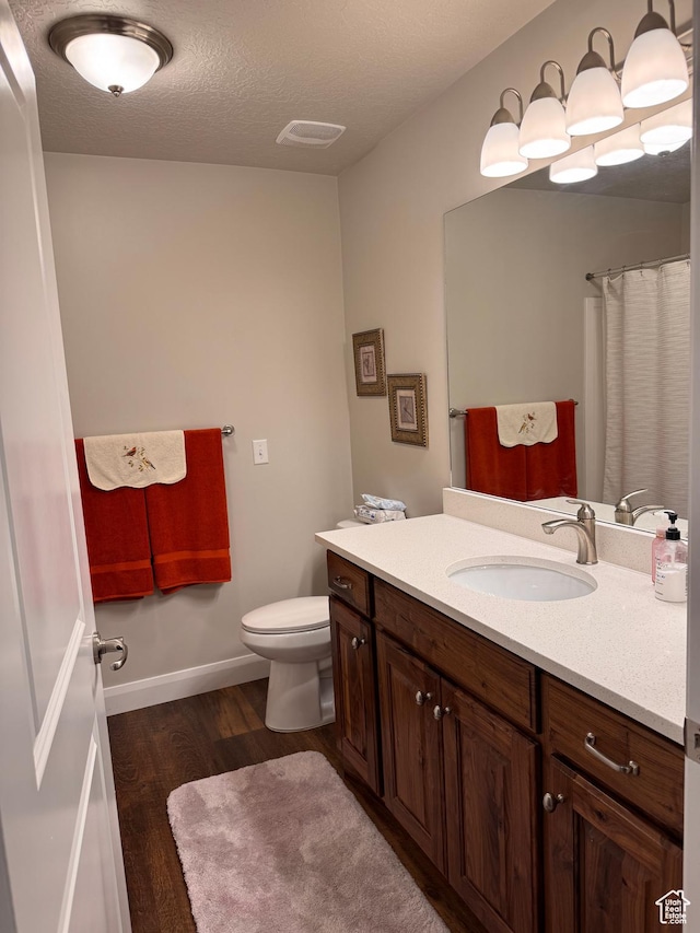 full bath with wood finished floors, vanity, baseboards, toilet, and visible vents