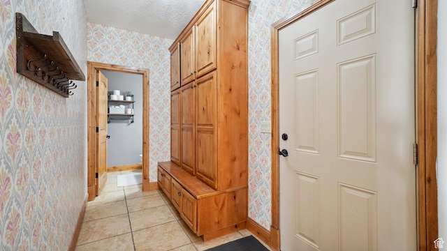 mudroom featuring baseboards, light tile patterned flooring, a textured ceiling, and wallpapered walls
