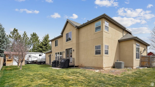 rear view of property with stucco siding, a yard, central AC, and fence