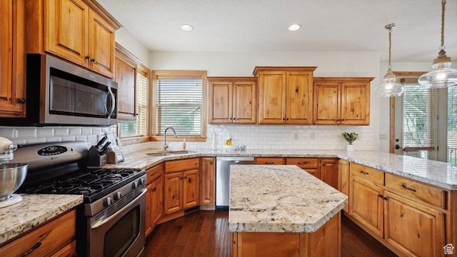 kitchen with a sink, a peninsula, brown cabinetry, appliances with stainless steel finishes, and dark wood-style flooring