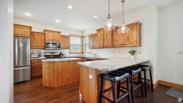 kitchen with a peninsula, a sink, brown cabinets, dark wood-type flooring, and appliances with stainless steel finishes