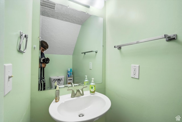 bathroom with lofted ceiling, visible vents, a sink, and a textured ceiling