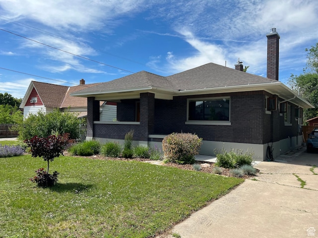 view of front of house featuring brick siding, roof with shingles, a chimney, and a front lawn