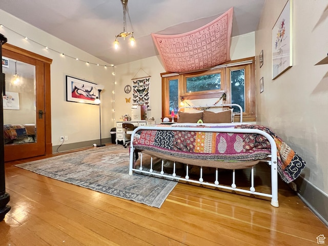bedroom with baseboards, vaulted ceiling, and hardwood / wood-style flooring
