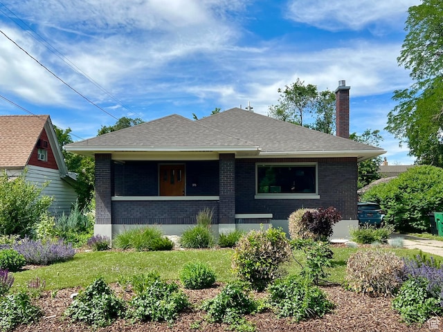 view of front of property with a front lawn, a chimney, covered porch, brick siding, and a shingled roof