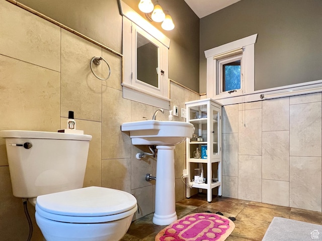bathroom with tile walls, a wainscoted wall, a sink, and toilet