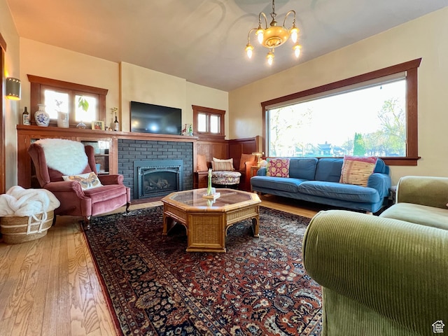 living area with an inviting chandelier, a brick fireplace, and wood finished floors