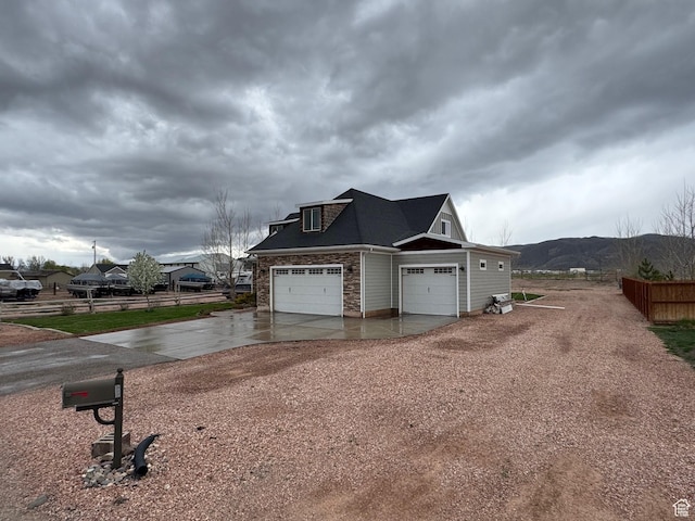 view of home's exterior featuring fence, a mountain view, driveway, and stone siding