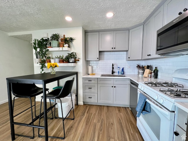kitchen with light wood-style flooring, appliances with stainless steel finishes, gray cabinets, and a sink