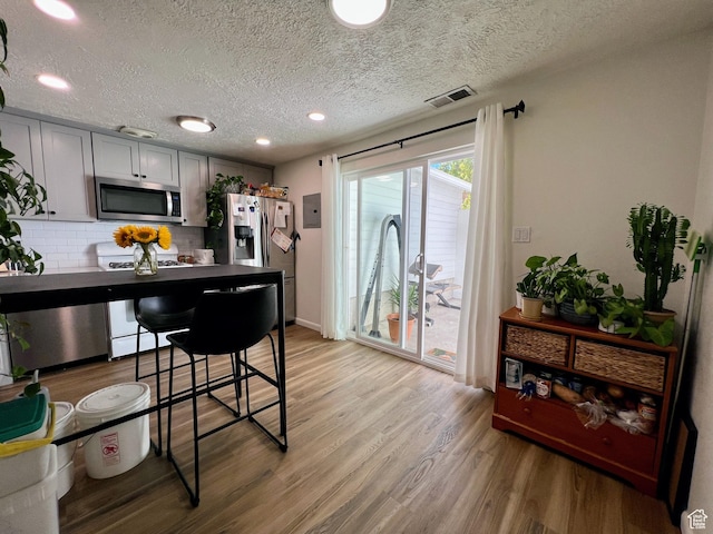 kitchen with a textured ceiling, decorative backsplash, stainless steel appliances, light wood-style flooring, and visible vents