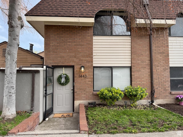 view of exterior entry with brick siding and roof with shingles