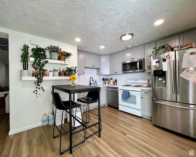 kitchen featuring light wood-style flooring, appliances with stainless steel finishes, gray cabinets, and a sink