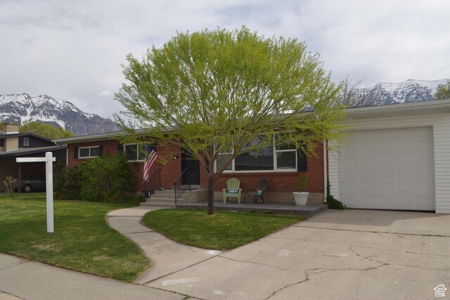 ranch-style house featuring a mountain view, concrete driveway, brick siding, an attached garage, and a front yard