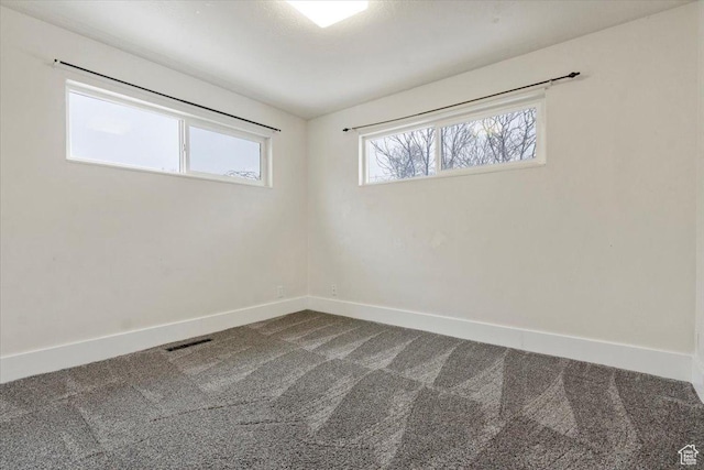 unfurnished room with baseboards, dark colored carpet, and visible vents