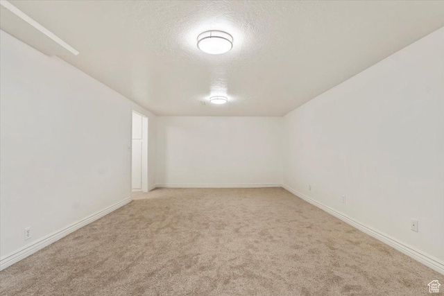 empty room with a textured ceiling, baseboards, and light carpet