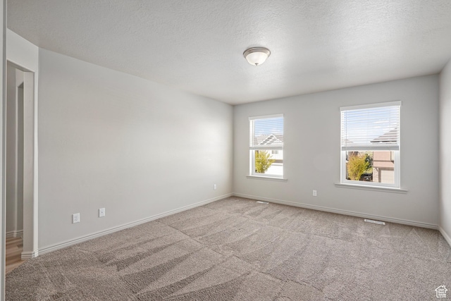 empty room with carpet, a textured ceiling, and baseboards