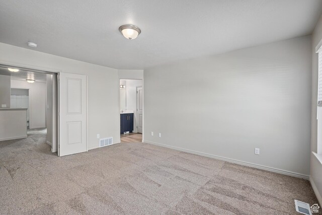 unfurnished bedroom with baseboards, ensuite bathroom, visible vents, and carpet